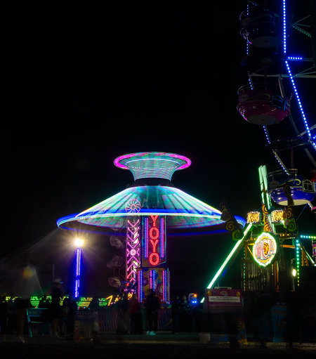 At night, amusement park rides are lit up. As one spins, the motion blur effect turns the glow into an illuminated conical shape.