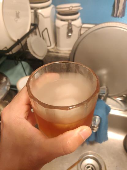 My left hand holding a tumbler glass with a smoked old fashioned drink, and the smoke is hovering right over the liquid inside the glass like a mist on a cold morning.