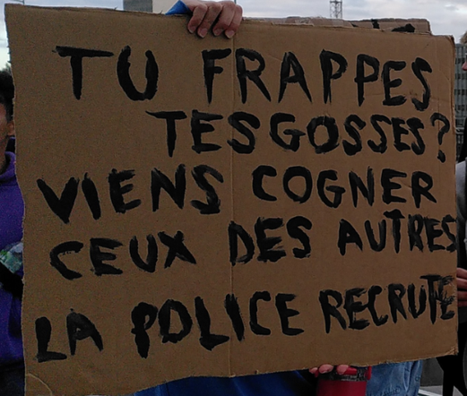 Photo d'une pancarte en carton avec une inscription en lettres majuscules noires. "Tu frappes tes gosses ? Viens cogner ceux des autres, la police recrute !"