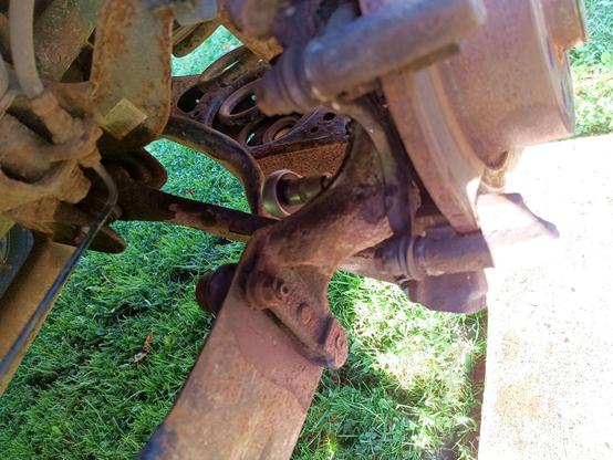 Bunch of rusty crusty bolts being undone on a rear left suspension. A ratchet spanner is in there somewhere with barely room to swing despite having first removed a support arm below it to even get it in at all.