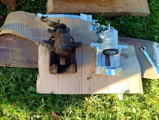 Same two brake calipers, other side. The old one has a damaged rubber bellow exposing the piston to air, road salt and corrosion. An open ring spanner is laying around next to it.