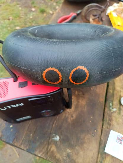 Inflated inner tube with two orange rimmed black rubber patches next to each other, looking like angry orange eyes. A tyre inflator is below it.