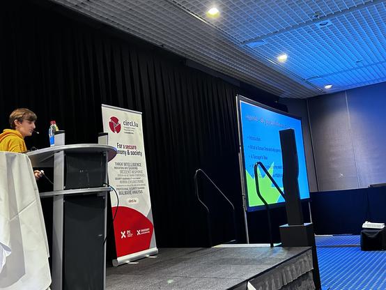 angled photo of a young person on stage behind a lectern on the left, with a screen on the right