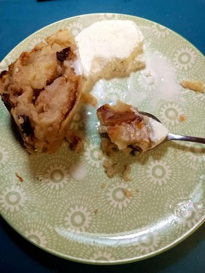An already half devoured plate of warm Apfelstrudel with cold vanilla ice cream. A spoon is laden with both, distracting the photographer.