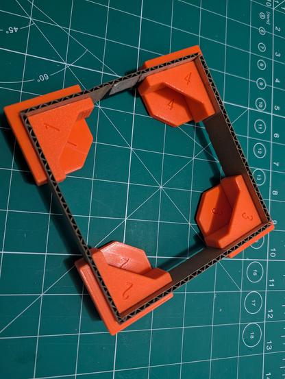 for strips of cardboard held together in a square shape by orange clamps.