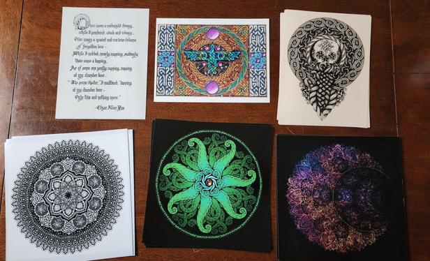 Six prints on a table, in various designs and colours; there's calligraphy, celtic knotwork, a skull, mandalas, tentacles